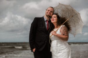 Braut im Boho Look und Schirm mit ihrem Ehemann vor der Nordsee am Inselstrand.