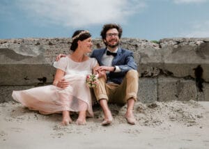 Lachendes Brautpaar sitzt vor der alten Kaimauer am Weststrand der ostfriesischen Insel Norderney.