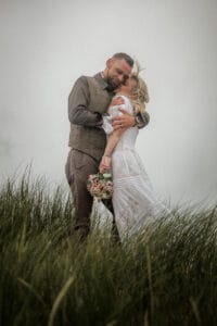 Feste Umarmung im Duenengras bei schlechtem Wetter bei einer Inselhochzeit.