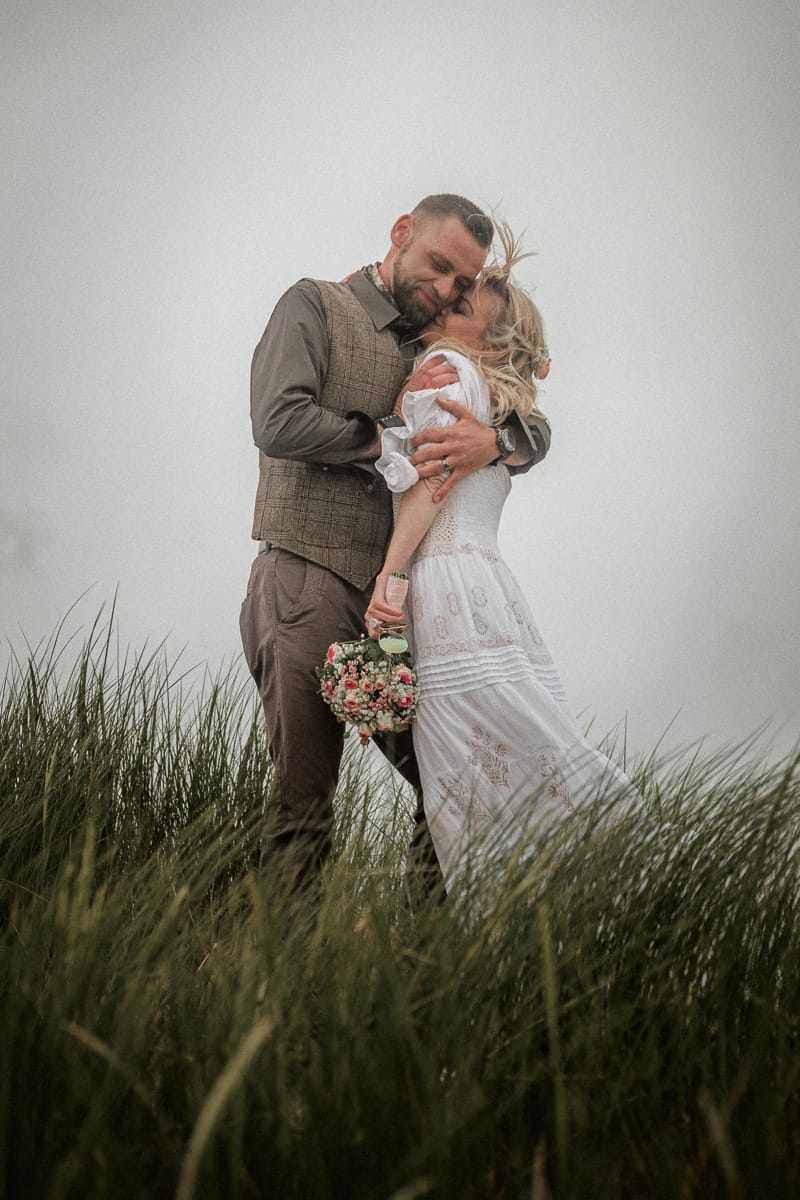 Feste Umarmung im Duenengras bei schlechtem Wetter bei einer Inselhochzeit.