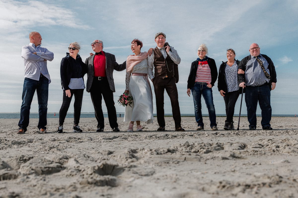 Gruppenportrait einer keinen Gesellschaft am leeren Strand am Vormittag.
