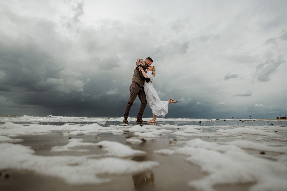 Ein Hochzeitskuss unter malerischem Himmel bei Ebbe am Weststrand.