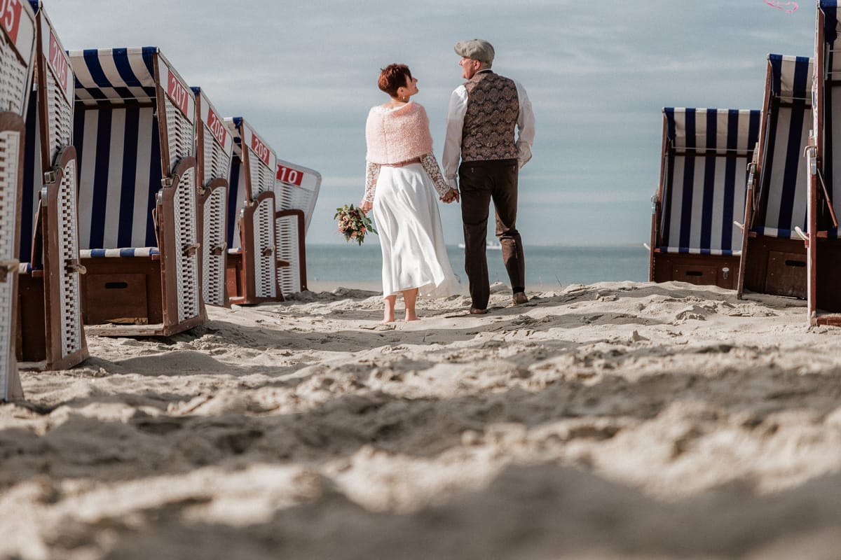 Brautpaar steht in einer Allee auf Strandkoerben bei ihrer Hochzeit auf der Insel.