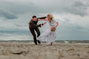 Ein rennendes junges Hochzeitspaar am Weststrand nahe des Badekarren bei schlechtem Wetter.