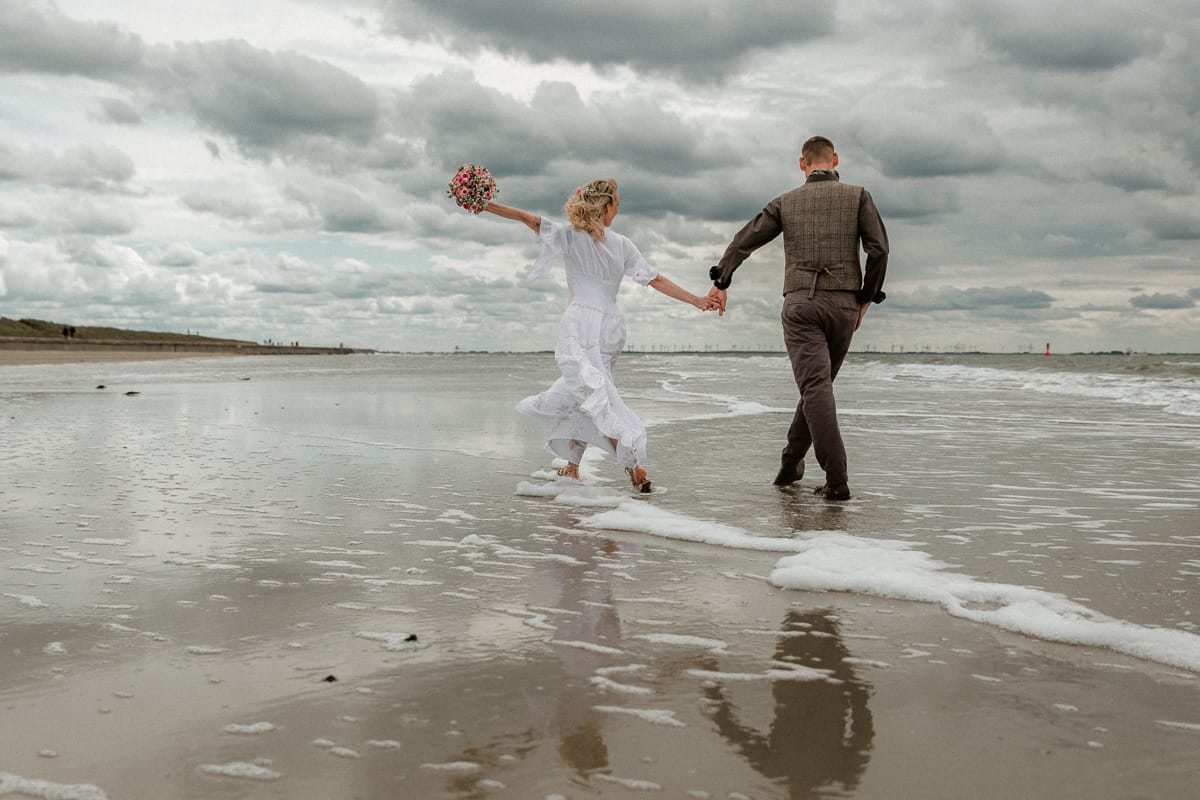 Bei epischem Himmel spaziert ein Brautpaar am Flutsaum am Weststrand der Insel Norderney.
