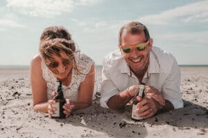 Lockeres Paarshooting auf Norderney liegend im Sand mit Sonnenbrille und Bier bei der Trauung.