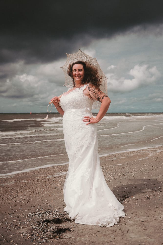 Eine Braut mit Tattoo und Sonnenschirm am Strand der Insel Norderney.