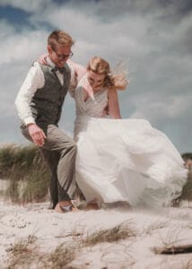 Brautpaar in wehendem Sand in den Duenen non Norderney stütz sich gegenseitig.