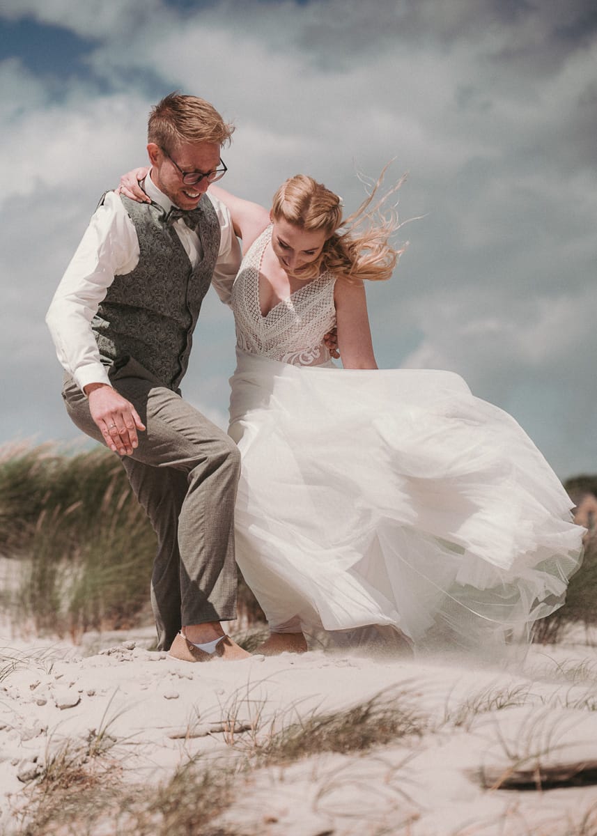Brautpaar in wehendem Sand in den Duenen non Norderney stütz sich gegenseitig.