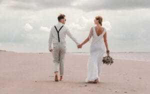 Hochzeitspaar geht am Strand von Norderney barfuß spazieren nach ihrer Trauung im Badekarren von Markus R. Hirsch ein Fotograf von Norderney.