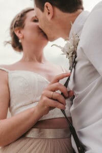 Eine Braut küsst den Bräutigam mit Hosentraegern bei ihrer Strandhochzeit auf Norderney.