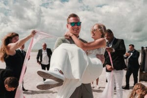Ein Brautigam traegt seine Braut bei der Hochzeit am Weststrand.