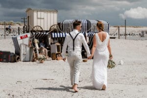 Ein Paar auf dem Weg zu ihrer Hochzeitsparty direkt in den Strandkoerben vor dem Badekarren.