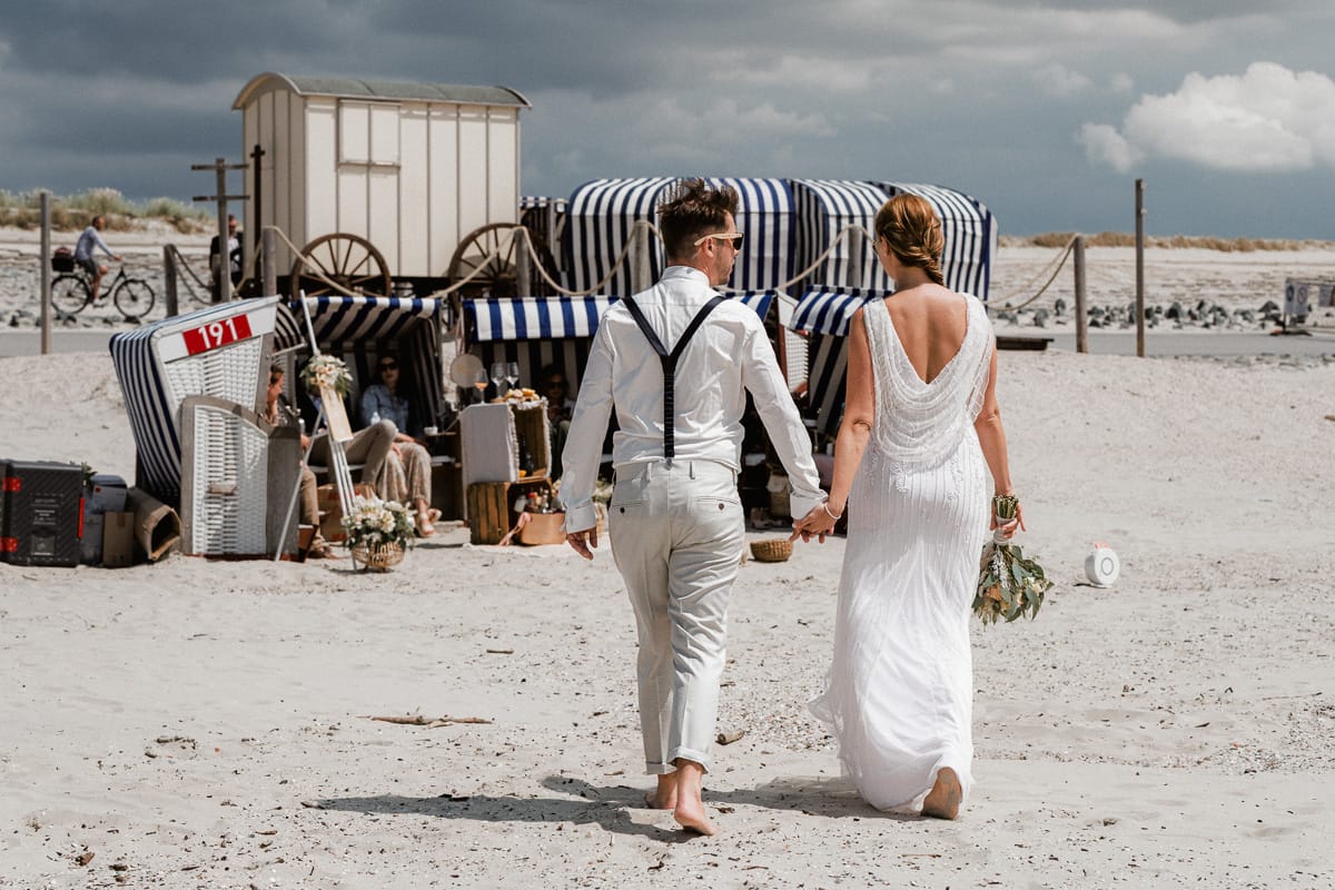 Ein Paar auf dem Weg zu ihrer Hochzeitsparty direkt in den Strandkoerben vor dem Badekarren.