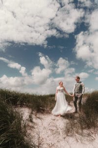 unter einem wunderschoenen Inselhimmel spaziert ein Brautpaar durch die Duenen an der Nordsee in Ostfriesland.