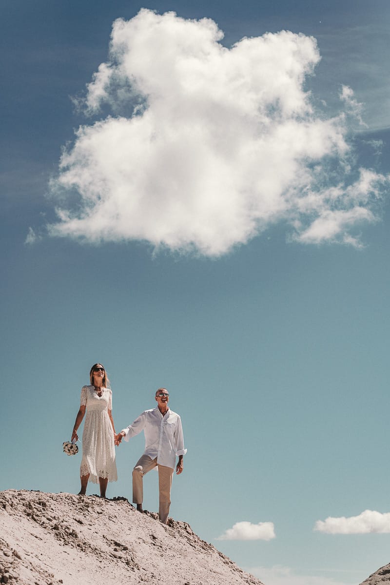 Ein Hochzeitspaar steht auf einer Duene unter einem blauen Himmel and der Nordsee.