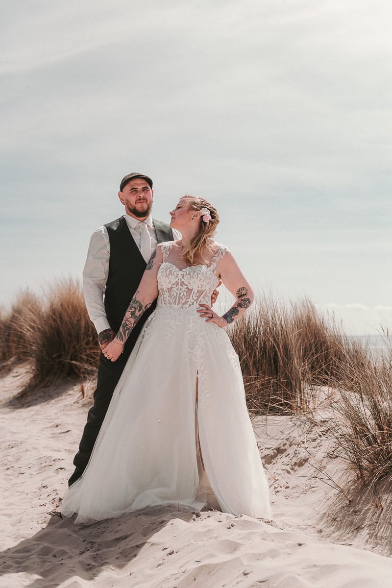 Ein Paar post laessig in den Duenen mit Tattoo und Schriebermuetze auf der Insel Norderney.