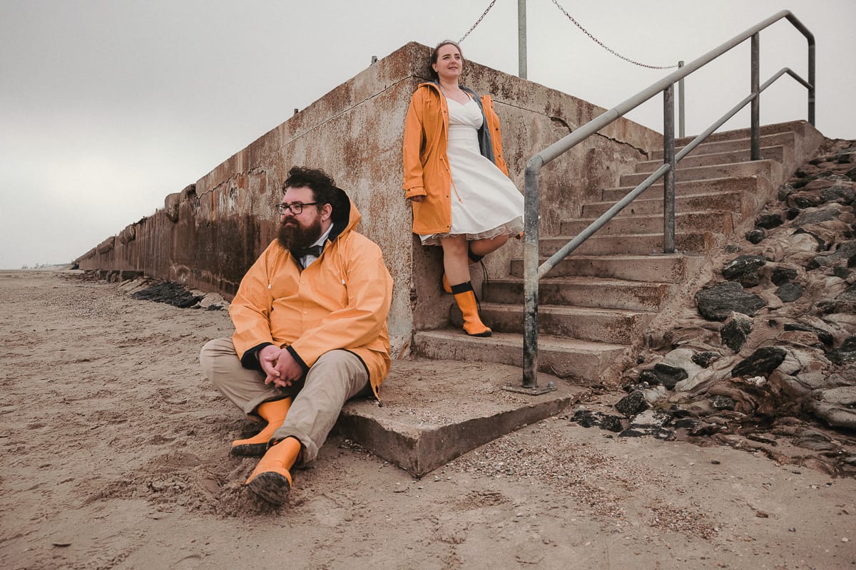 Ein Hochzeits Shooting am Strand bei regen bei dem das Paar Friesennerze traegt.