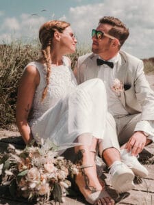 Brautstrauss und Hochzeitspaar mit Sonnenbrillen sitzend auf einem Steg am Weststrand.