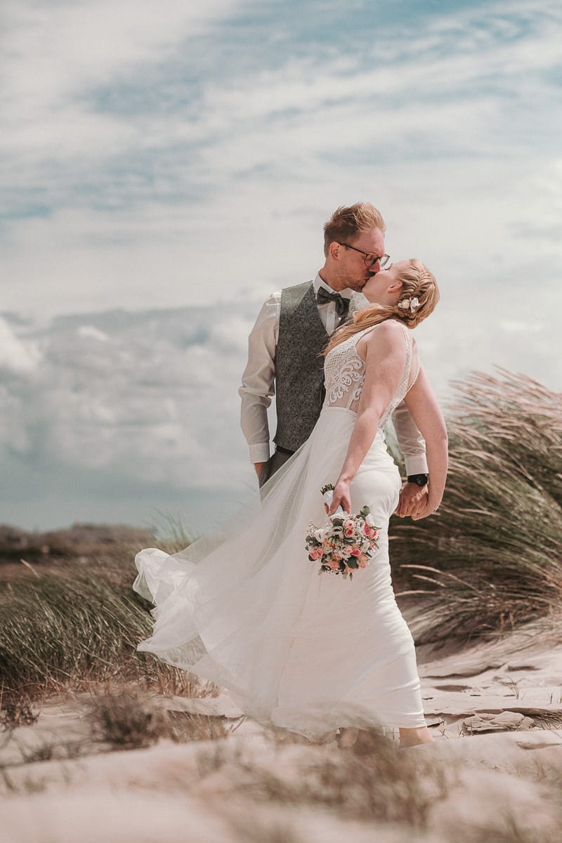Ein Kuss in den Duenen nach der Hochzeit im Badekarren vom Fotografen Hirsch.