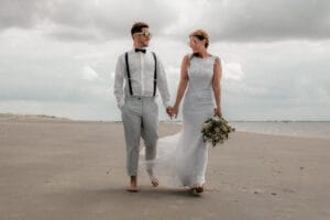 Hochzeitspaar geht am Strand von Norderney barfuß spazieren nach ihrer Trauung im Badekarren von Markus R. Hirsch ein Fotograf von Norderney.