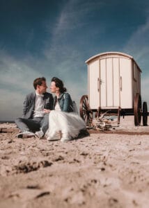 Das Hochzeitspaar sitzt alleine vor dem Badkarren auf Norderney unter blauem Himmel.